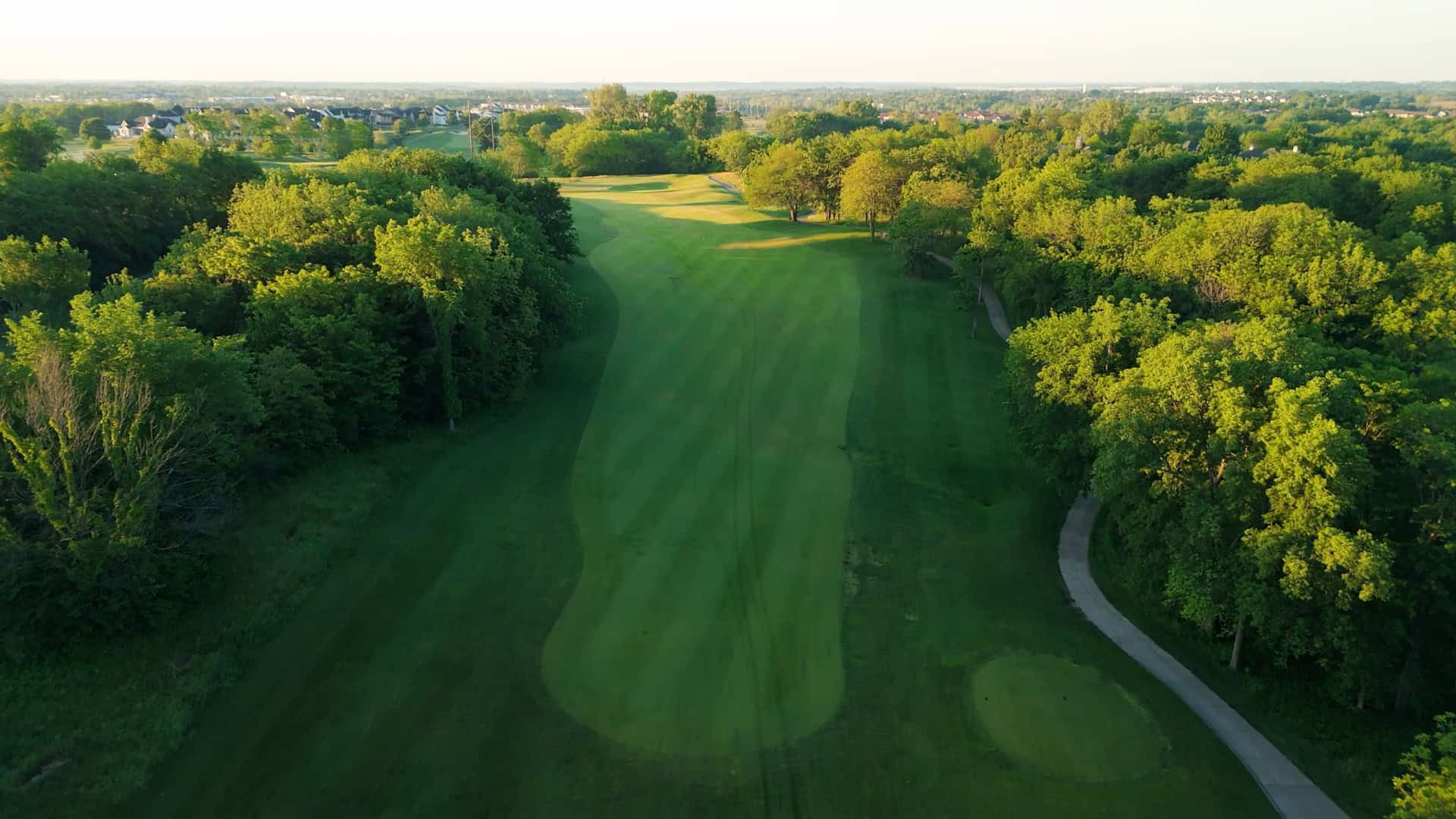Cinematic drone shot of a pristine golf course green at sunset